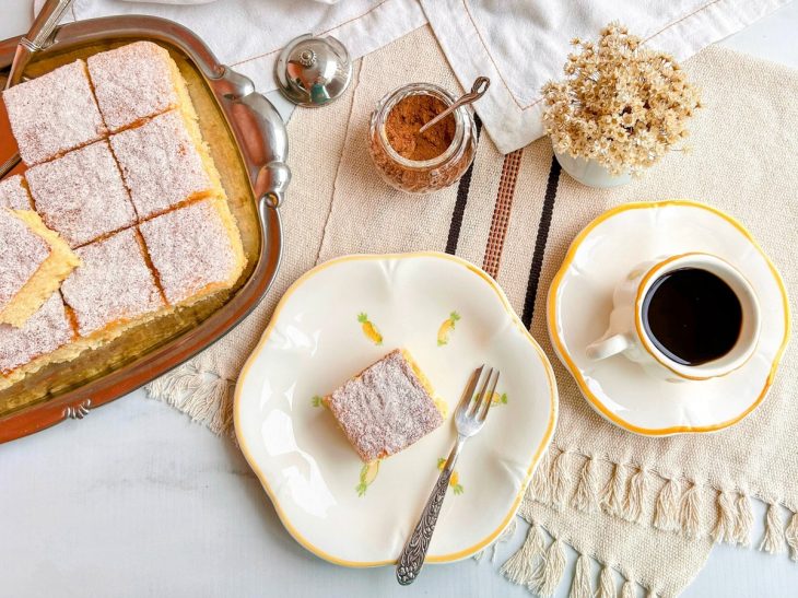 Bolo pronto, pedaço servido em prato, xícara de café servida ao lado.