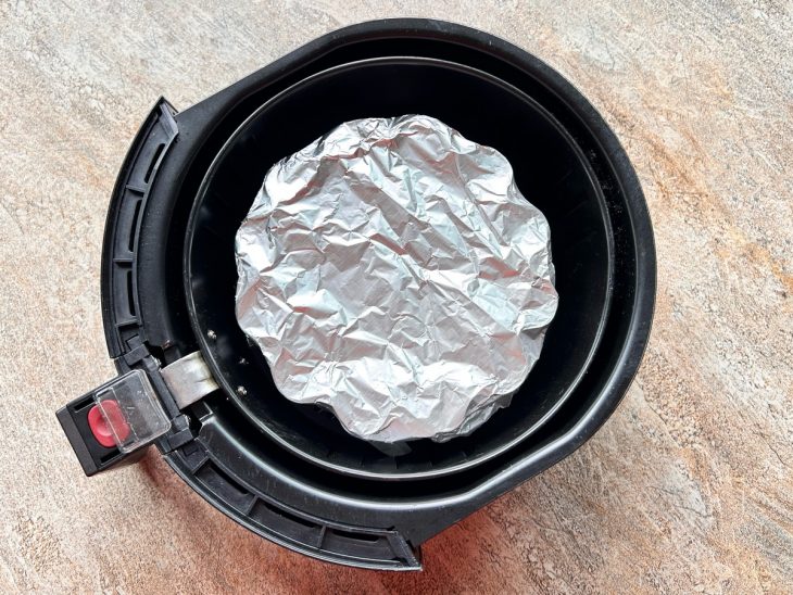 Forma coberta com papel alumínio e disposta no cesto da airfryer.