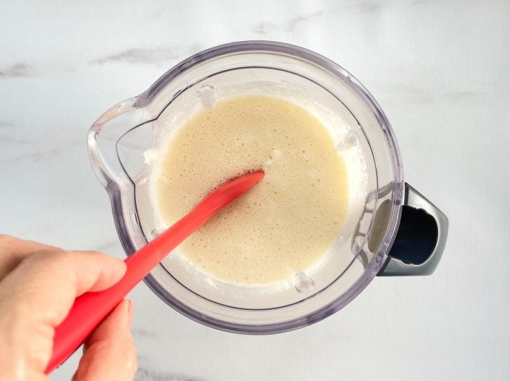 Um liquidificador com a mistura de ovos, açúcar, iogurte natural, arroz demolhado, o óleo, sal, fermento e coco ralado.