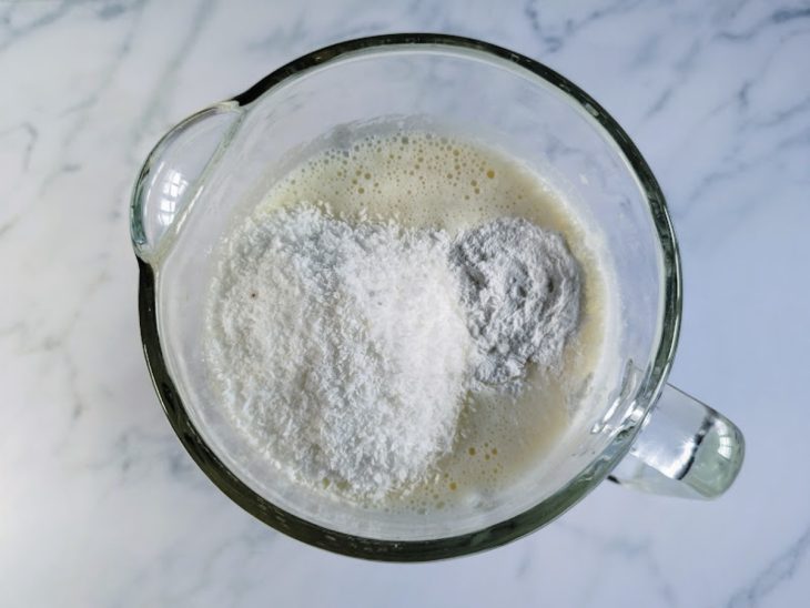 Um liquidificador com ovos, arroz, leite condensado, leite, óleo, coco ralado e fermento.
