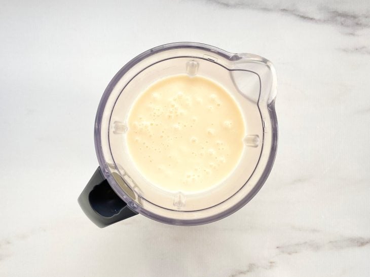Um liquidificador com ovos, arroz cozido, leite de coco, óleo e açúcar.