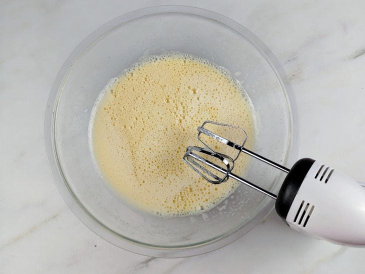 Ingredientes batidos em uma tigela de vidro com auxílio de uma batedeira.