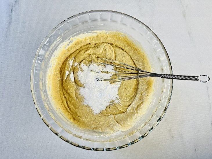 Mistura acomodada em uma tigela de vidro com farinha de trigo e fermento adicionados.