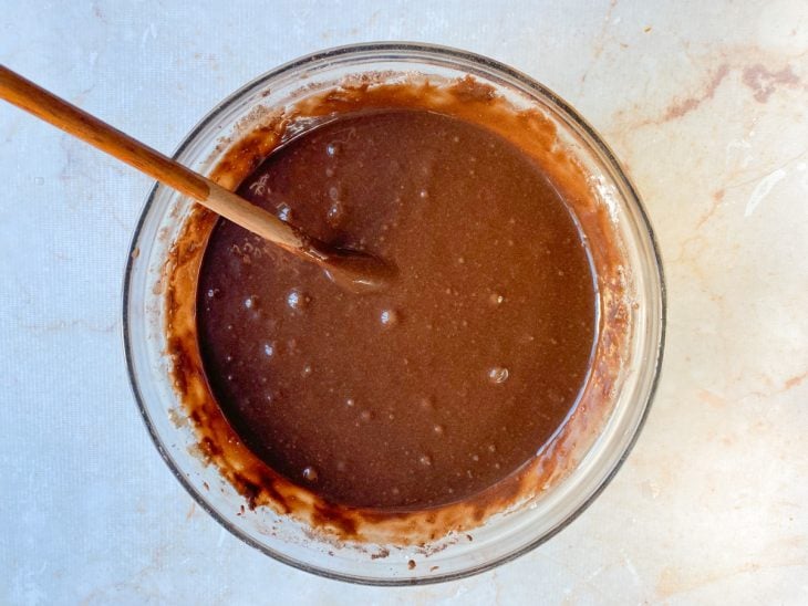 Mistura do liquidificador transferida para uma tigela redonda de vidro com farinha de trigo e chocolate em pó incorporados.
