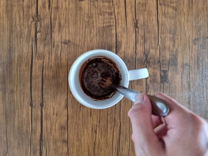 Cacau e canela adicionados na caneca branca com uma colher misturando.