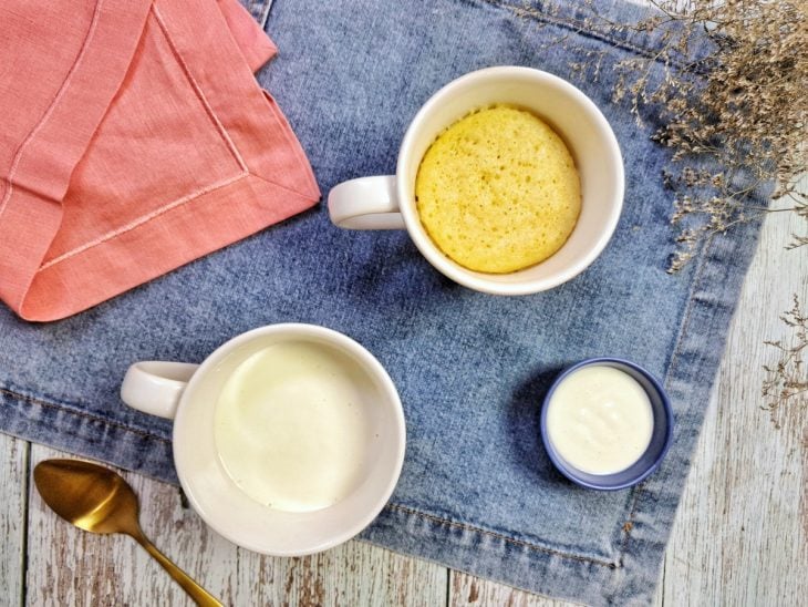 Bolo de caneca e pote com creme de iogurte sobre uma mesa.