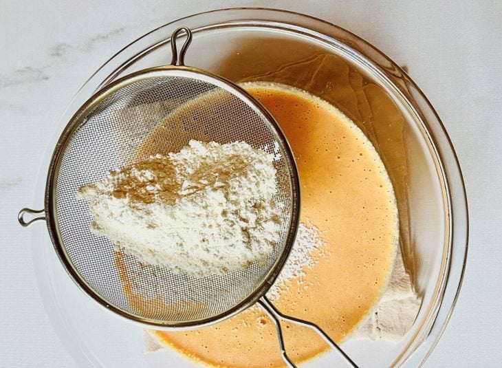 Mistura do liquidificador em uma tigela de vidro junto com farinha peneirada.