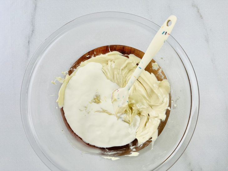 Chocolate branco derretido e creme de leite misturados em um recipiente de vidro.
