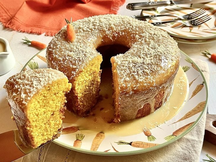 Bolo de cenoura com cobertura de chocolate branco pronto para consumo sobre uma boleira.