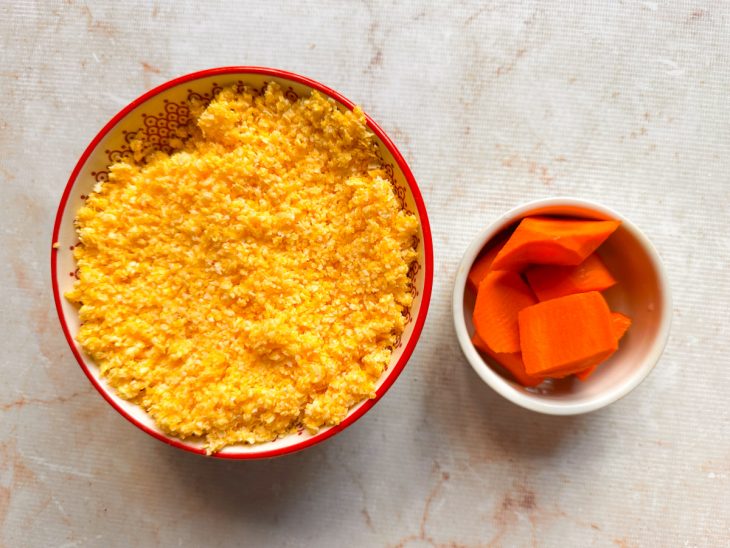 Flocão de milho sendo hidratado com água em uma tigela e cenouras cortadas.