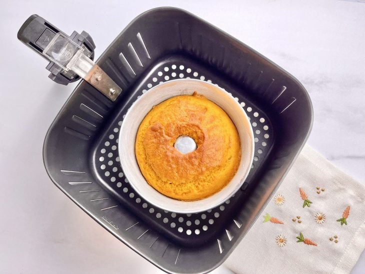 Uma cesta de airfryer com uma forma contendo bolo de cenoura.