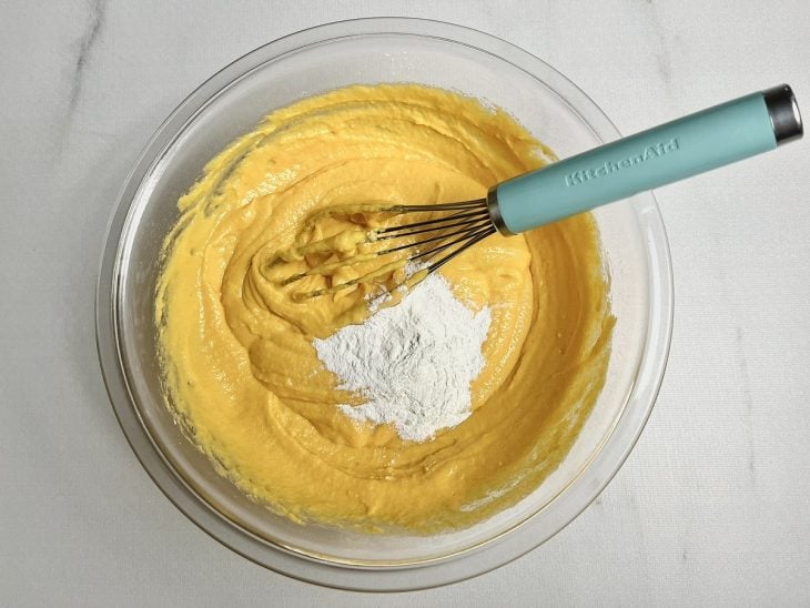 Mistura colocada em uma tigela de vidro com ingredientes adicionados e incorporados por um fouet (batedor de arame).