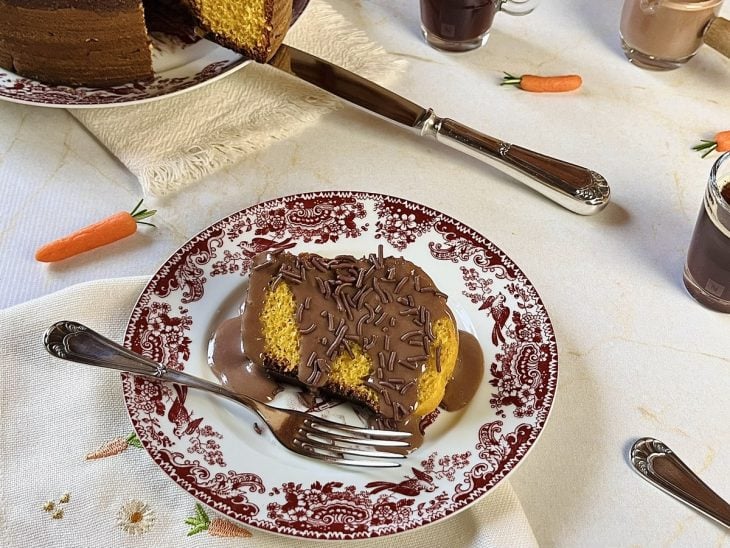 Fatia de bolo servida em um prato com calda de chocolate despejada.