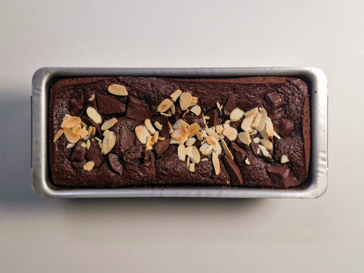 Bolo sendo finalizado com chocolate picado e rodelas de banana antes de assar.