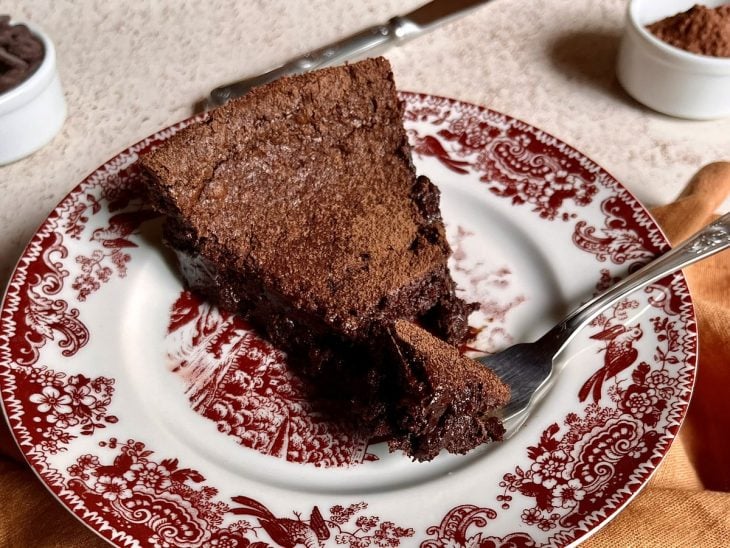 Um recipiente contendo um pedaçp de bolo de chocolate molhadinho.