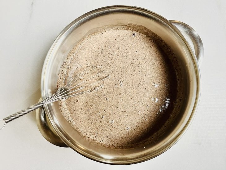 Leite condensado, creme de leite, gema peneirada, chocolate meio amargo, chocolate em pó e amido dissolvido com leite misturados em uma panela.