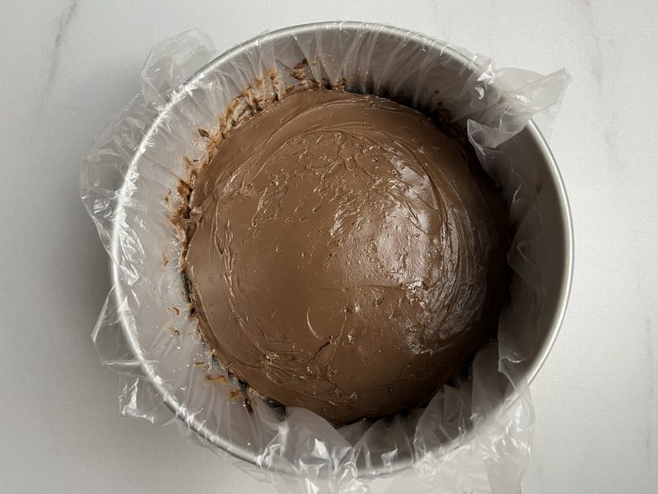 Camada de creme de chocolate meio amargo espalhada sobre a primeira parte do bolo.