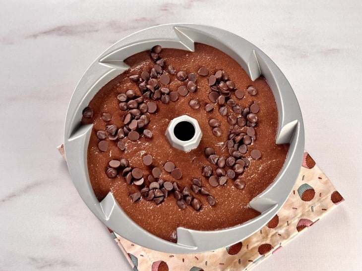 Forma redonda com furo no meio com massa de bolo crua com chocolate salpicado por cima.