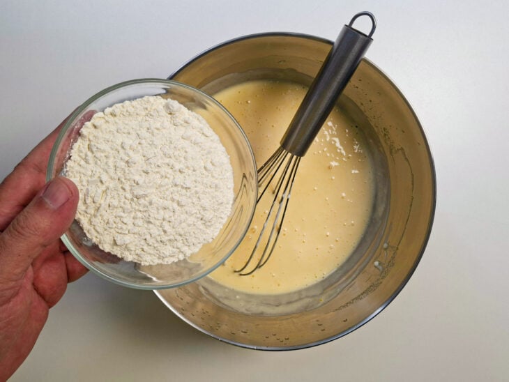 Farinha de trigo sendo peneirada e mexida delicadamente na massa com o batedor de arame.