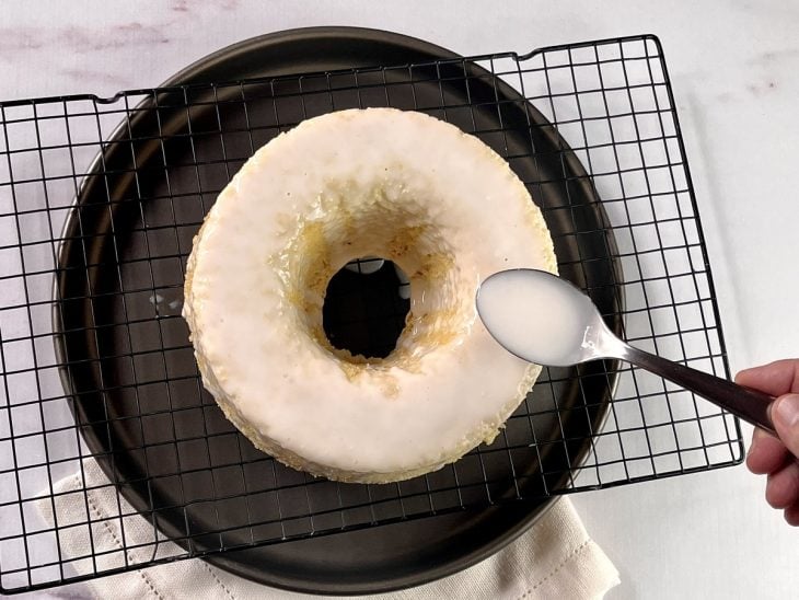 Uma forma contendo bolo de coco sendo coberto com a cobertura.