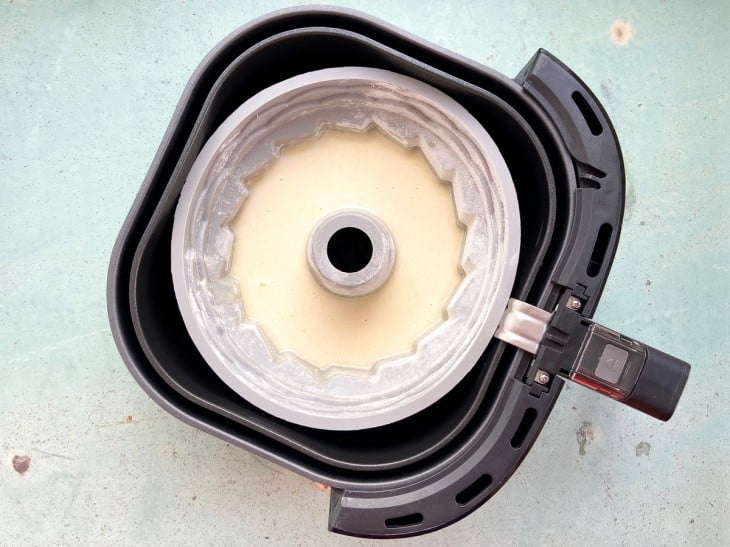 Uma cesta de airfryer com uma forma redonda contendo a massa do bolo.