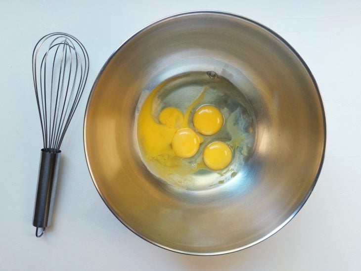 Um fouet e um recipiente contendo 4 ovos crus.