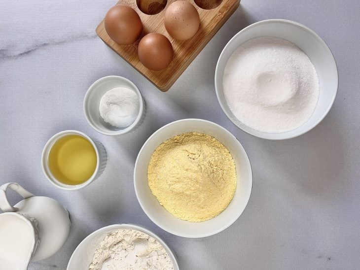 Ingredientes para a receita de bolo de fuba simples e fácil reunidos em uma bancada.