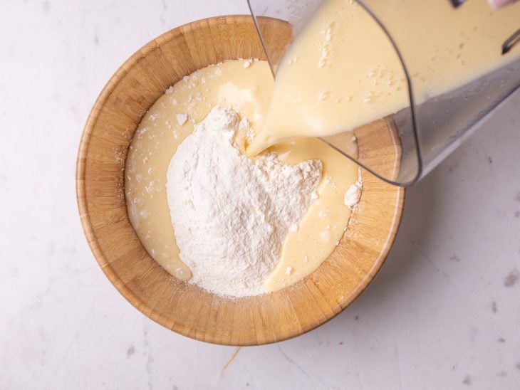 Mistura do liquidificador despejada em um recipiente com farinha de trigo.