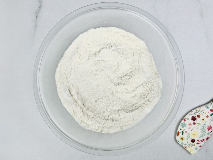 Farinha de trigo e açúcar misturados em uma tigela de vidro redonda.