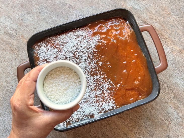 Uma forma com o bolo assado, coberto com caramelo e coco ralado.