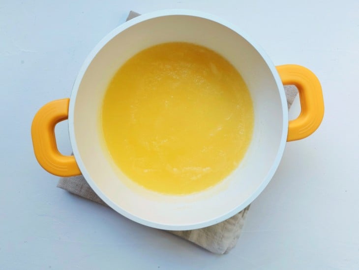 Ingredientes da calda misturados homogeneamente dentro de uma panela na cor branca e alças na cor amarela.
