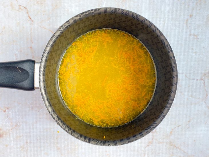Numa panela, o açúcar, as raspas da laranja e o suco.