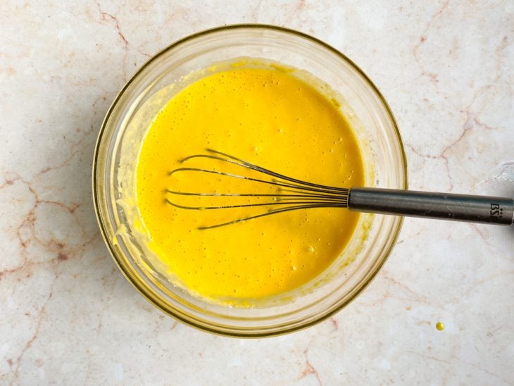 Uma tigela com ovos, açúcar, suco de laranja, óleo e farinha batidos com fouet.