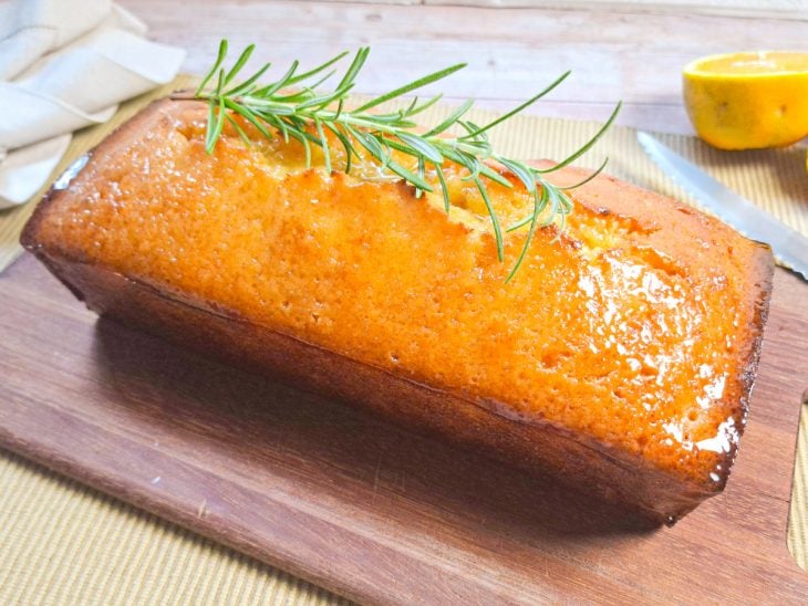 Bolo de laranja sem liquidificador pronto para consumo e finalizado com um ramo de alecrim.