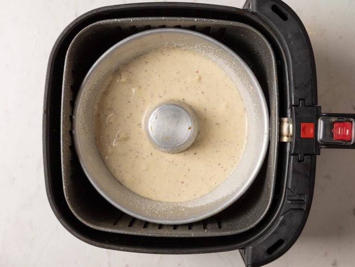 Forma com massa de bolo dentro do cesta da air fryer.