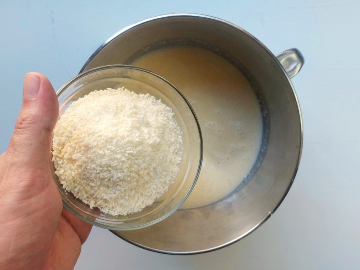 Uma tigela com a mistura dos ingredientes da massa do bolo de mandioca e a adição de coco ralado.