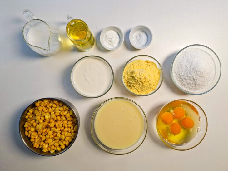 Bancada organizada com ovos, milho escorrido, fubá, coco ralado e demais ingredientes.