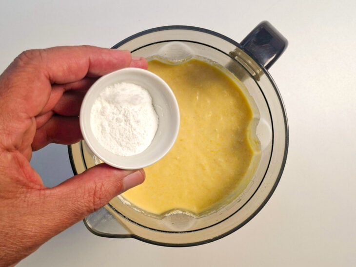 Fermento químico em pó sendo adicionado sobre a massa batida no liquidificador.