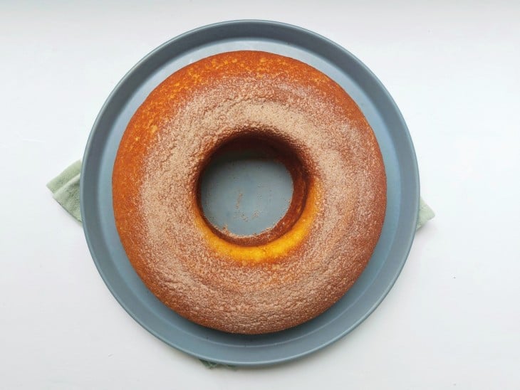 Bolo desenformado em um prato grande de cor azulada com açúcar polvilhado por cima.