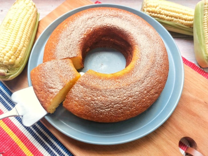 Bolo de milho molhadinho pronto com um pedaço sendo cortado.