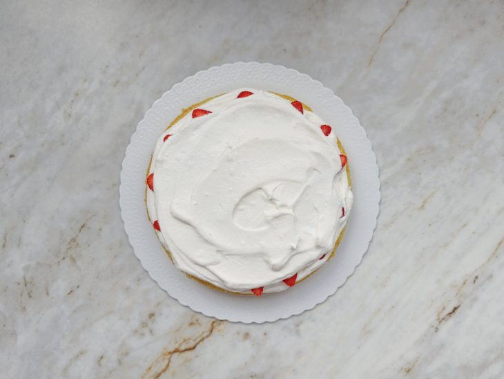 Chantlly e morangos distribuídos sobre o bolo.