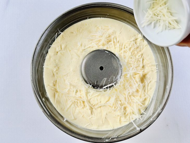 Na forma, parmesão ralado sendo polvilhado sobre a massa.