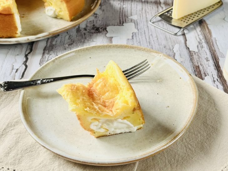 Fatia do bolo pão de queijo servida em prato, garfo acompanhando completa o quadro.