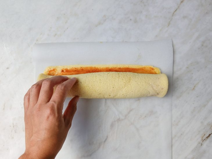 Massa sendo enrolada sobre uma folha de papel-manteiga.