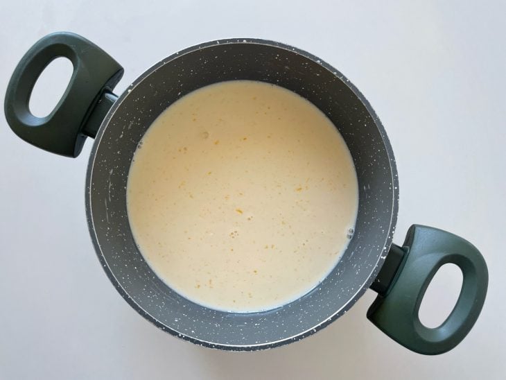Mistura de leite condensado, gemas peneiradas e leite sendo preparada na panela.