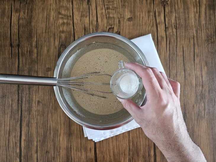 fermento sendo adicionado à tigela com ingredientes líquidos escuros.