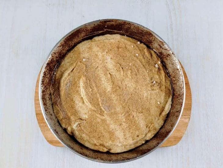 Massa despejada na forma com açúcar e canela polvilhados na superfície.