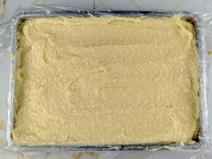 Recheio adicionado sobre uma parte da massa acomodada em uma forma forrada com plástico.