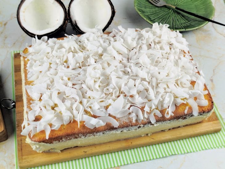 Bolo gelado de coco recheado desenformado, finalizado com lascas de coco e pronto para servir.