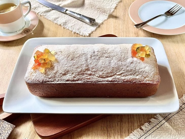 Bolo inglês finalizado com açúcar de confeiteiro e frutas cristalizadas, pronto para servir.